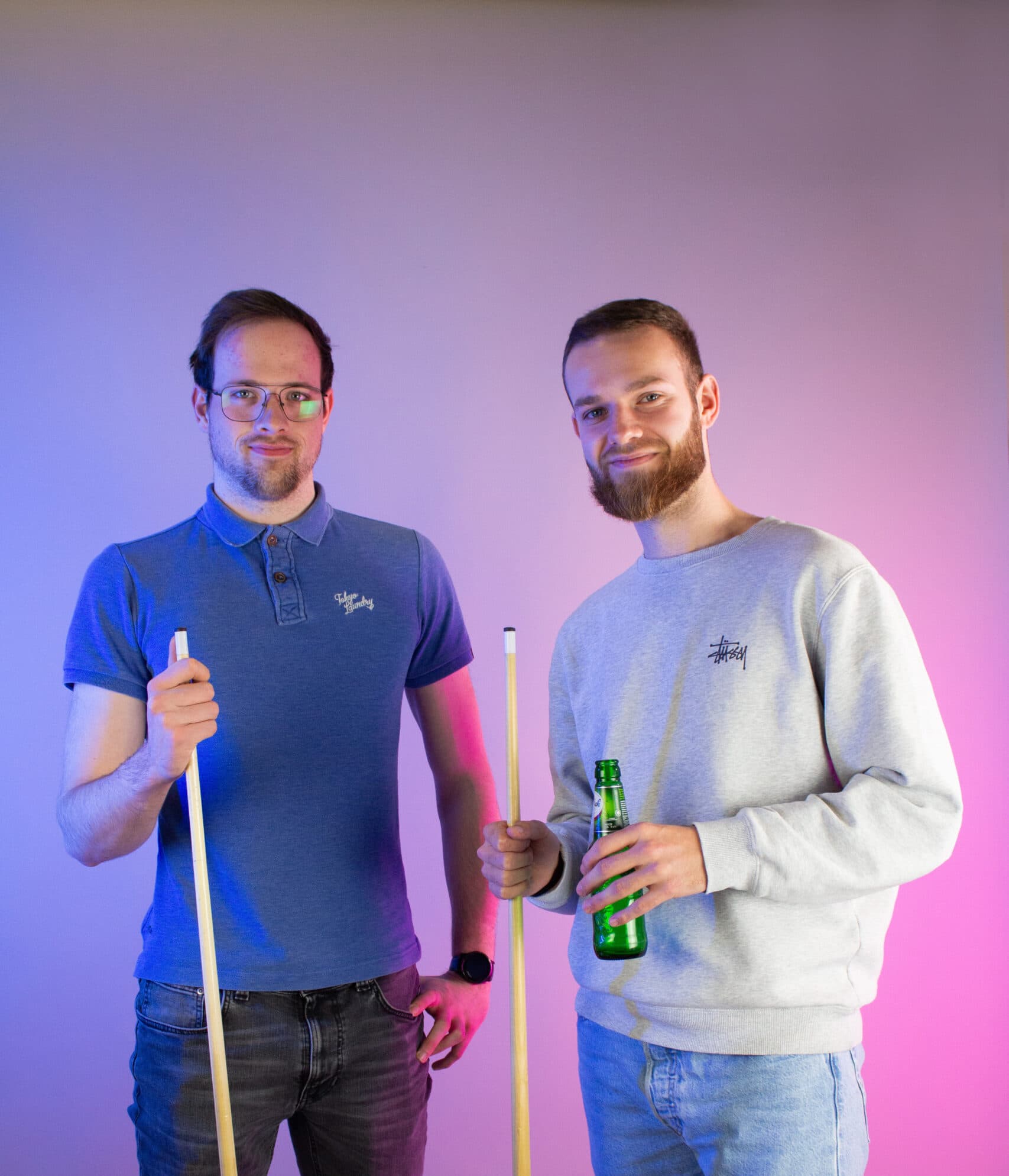 Thimo en mick lachen in de camera, mick houdt een biertje vast en beiden houden de keu van een pooltafel vast